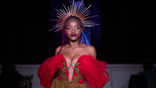 Fashion model wearing a crown that looks like rays of light and a red and green gown.