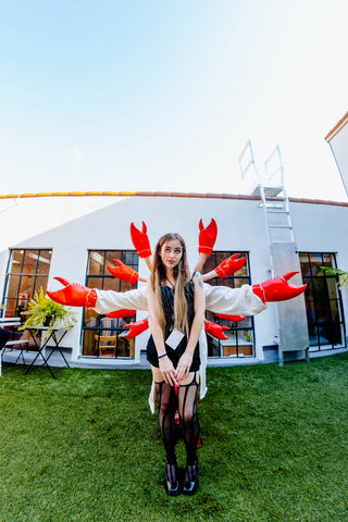 Model posing like Shiva with many arms that have lobster claws for hands.