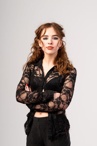 Model standing with arms crossed, wearing a black lace top by fashion designer Cardiovascuwhore.