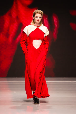 Model walking down a runway wearing a red dress by fashion designer Cardiovascuwhore.