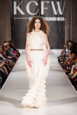 Model walking down runway wearing a white frilly dress from fashion brand SKYE|AIRE.