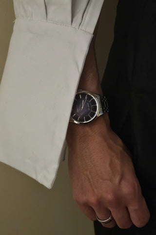 Detail shot of a person's arm wearing a watch with a large white shirt cuff.